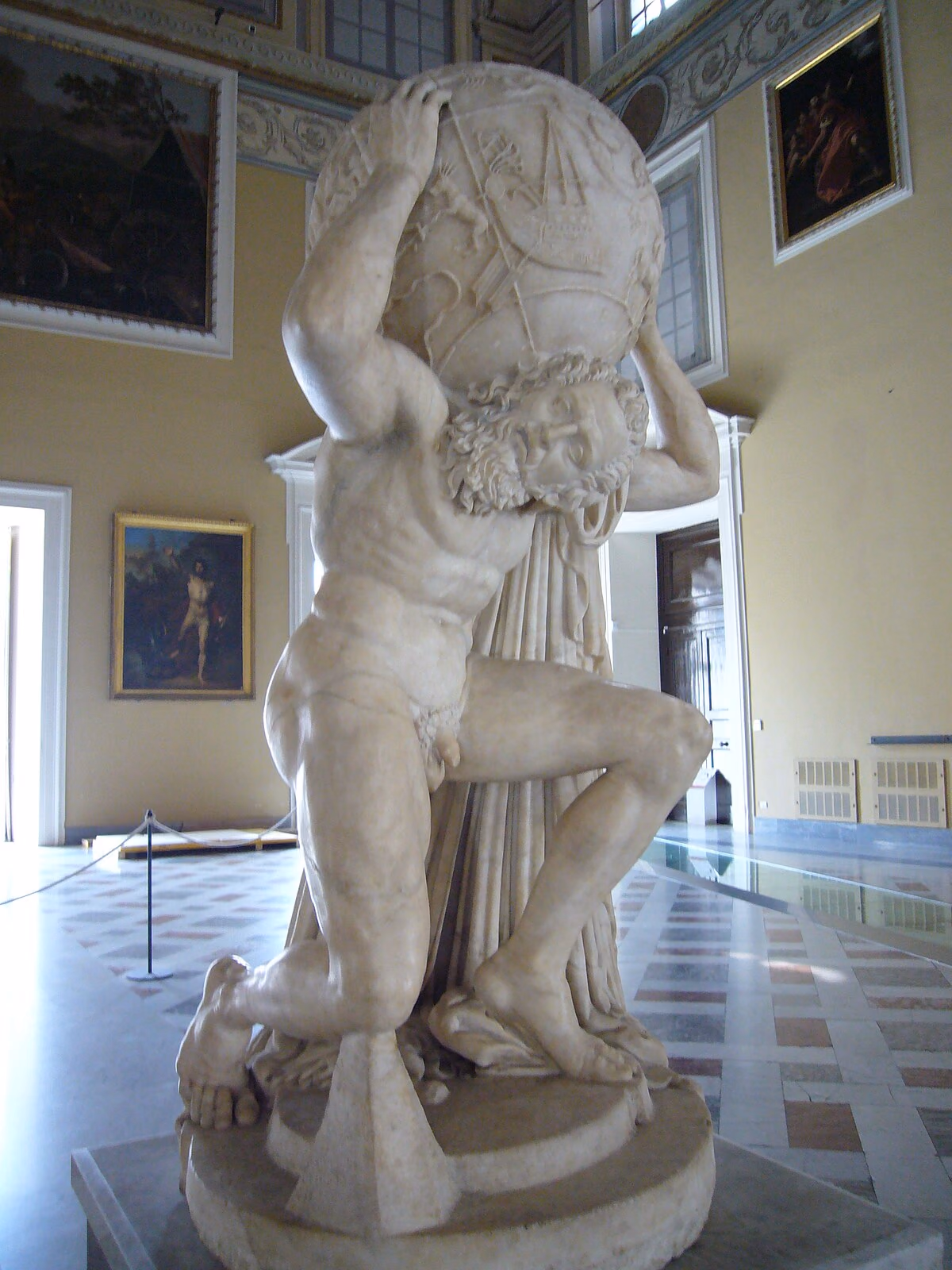 The marble Farnese Atlas statue kneeling under a celestial globe carved with constellation figures, in the Naples archaeological museum.