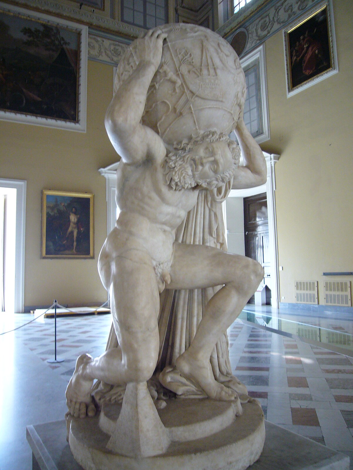 The marble Farnese Atlas statue kneeling under a celestial globe carved with constellation figures, in the Naples archaeological museum.