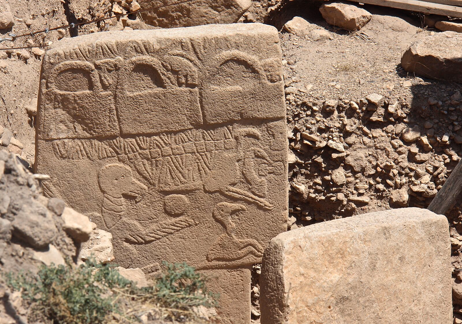 The Vulture Stone, Pillar 43 at Göbekli Tepe, a carved limestone pillar with vulture, scorpion, and bag-shaped reliefs, standing in the excavation.