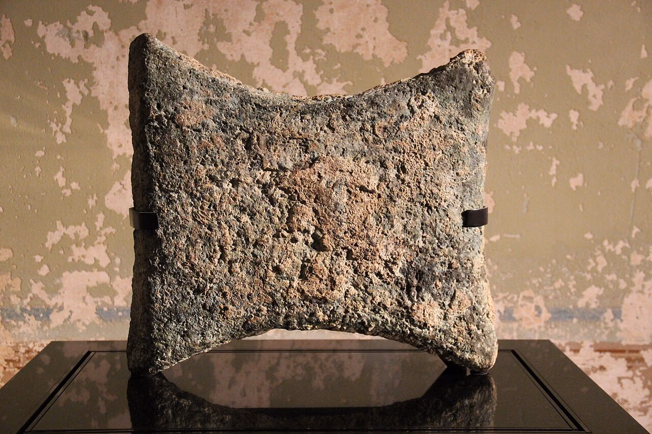 An ancient copper oxhide ingot displayed as a flat rectangular trade object with corner handles.