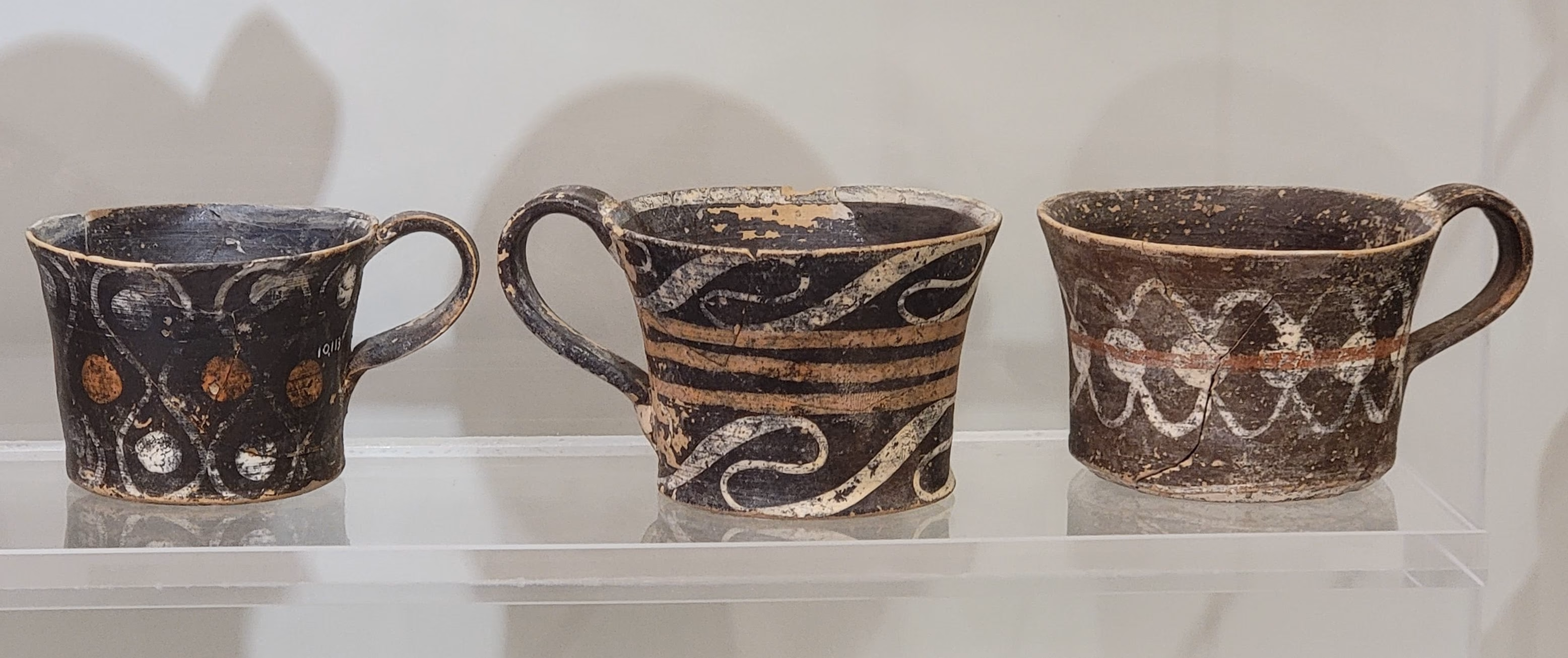 Minoan Kamares pottery cups with orange and cream decoration on a dark museum background.