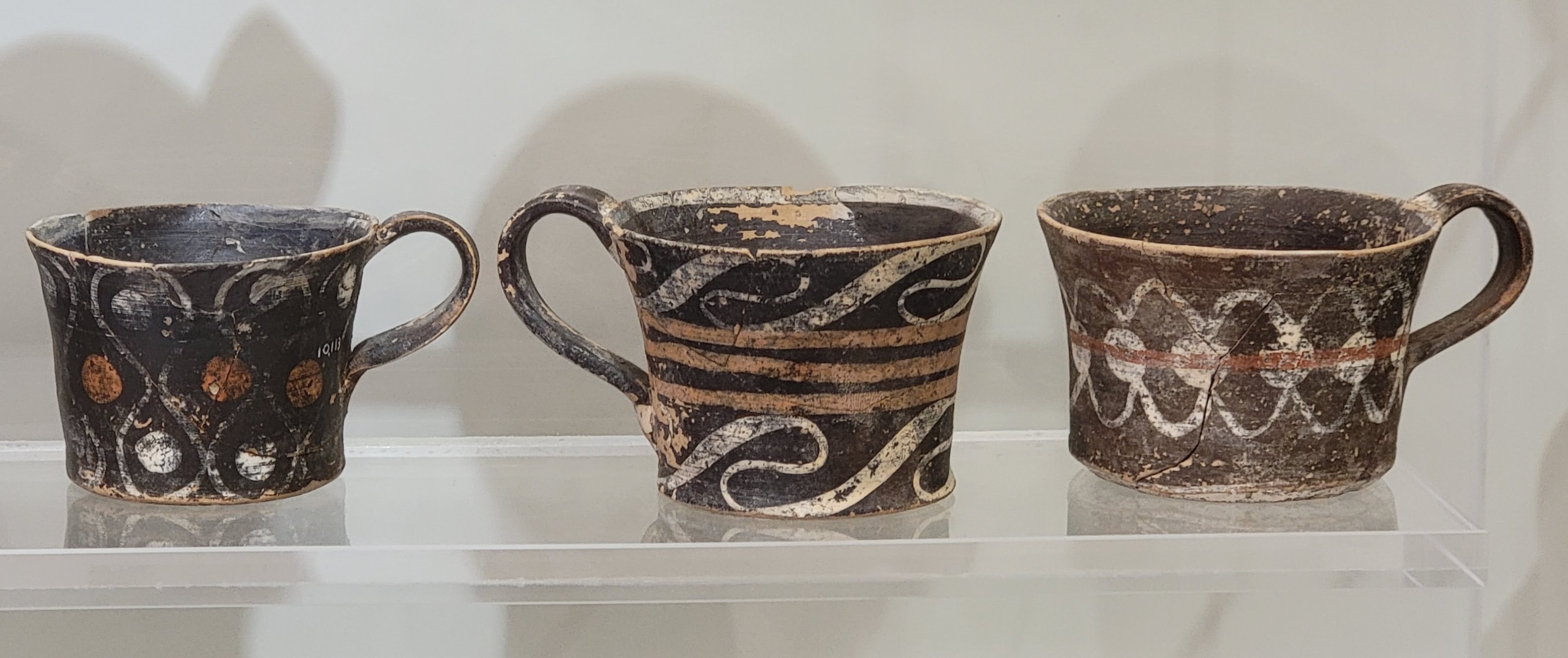 Minoan Kamares pottery cups with orange and cream decoration on a dark museum background.